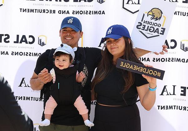 Two adults with a baby posing in front a step and repeat for Admissions and Recruitment.